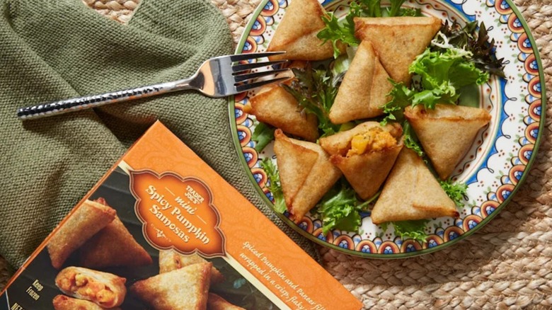 Box of mini spicy pumpkin samosas alongside a plate with the fully prepared product and salad greens