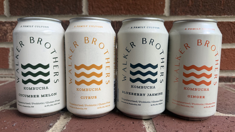 Four cans of Walker Brothers kombucha in different flavors lined up on brick surface