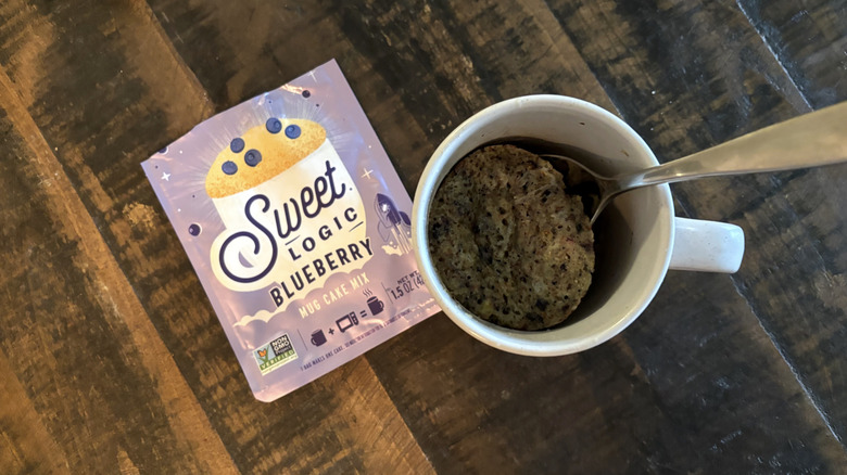 Sweet Logic blueberry mug cake in package and mug on wooden table.