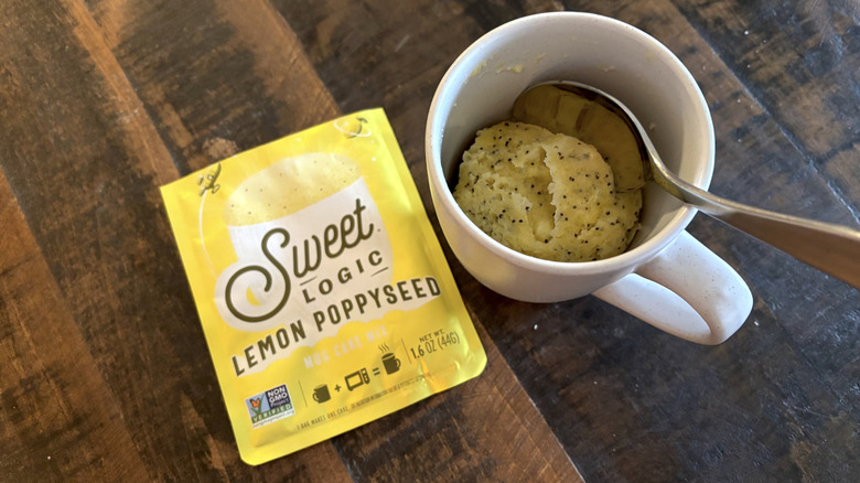 Sweet Logic lemon poppy seed mug cake in package and mug on wooden table.
