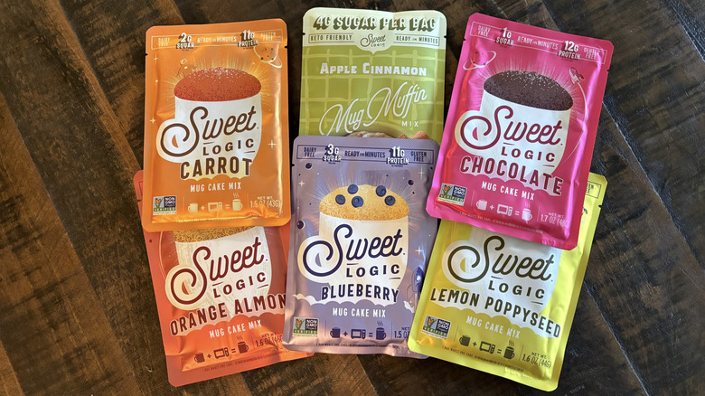 A variety of Sweet Logic mug cakes in packages on a wooden table.