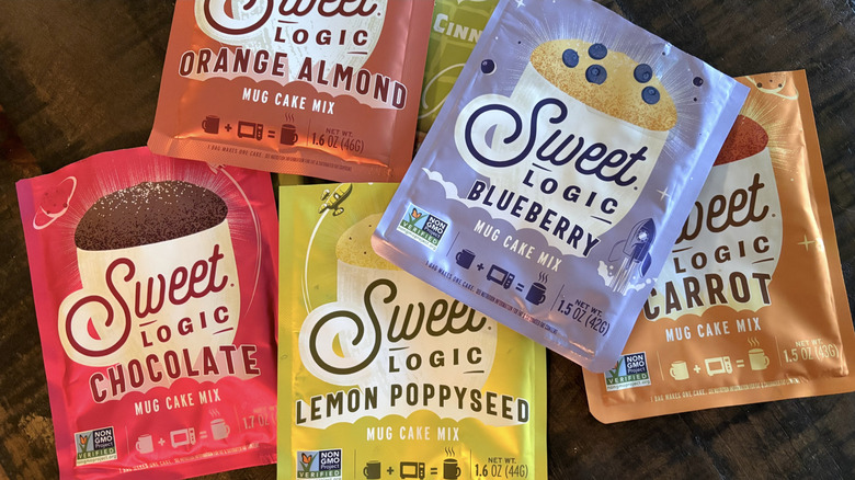 A variety of Sweet Logic mug cakes in packages on a wooden table.