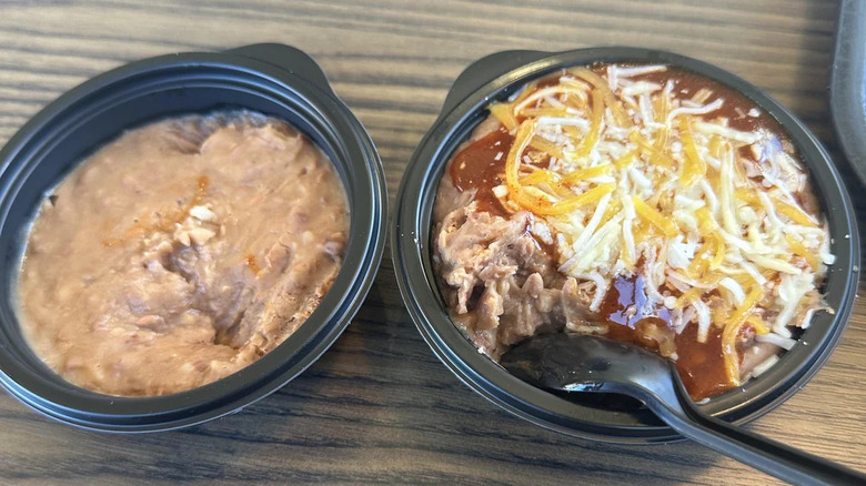 Two black containers on a table, one with refried beans and one with beans and cheese