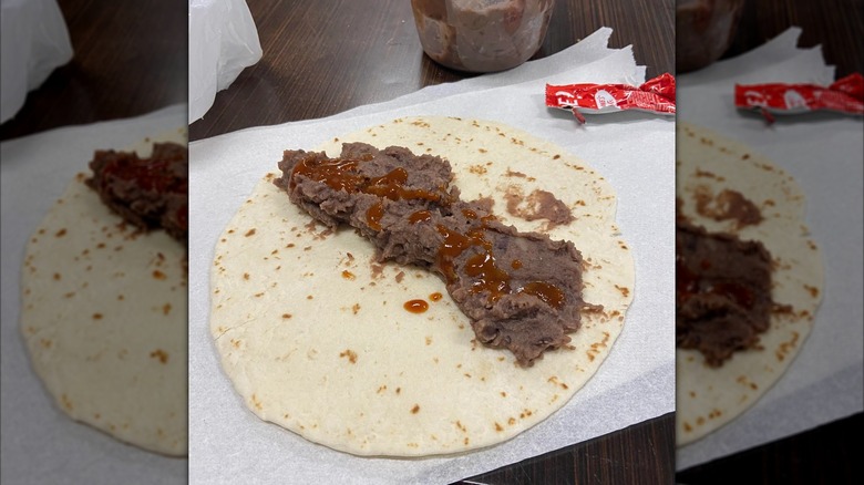 Open tortilla with refried beans and sauce on a table, mirrored image