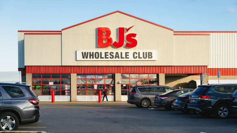 Multiple cars parked in an asphalt lot in front of the red-arched doorway to a BJ's Wholesale Club.
