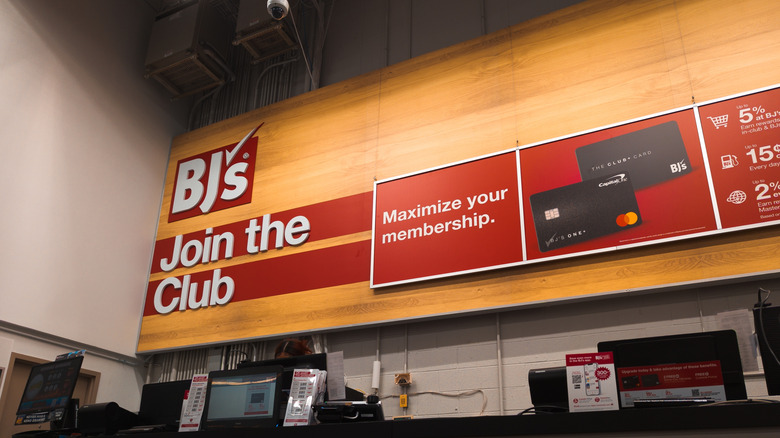 A red sign on a wood-paneled wall reads, "BJ's: Join the Club, Maximize your membership," alongside images of two BJ's Mastercards.