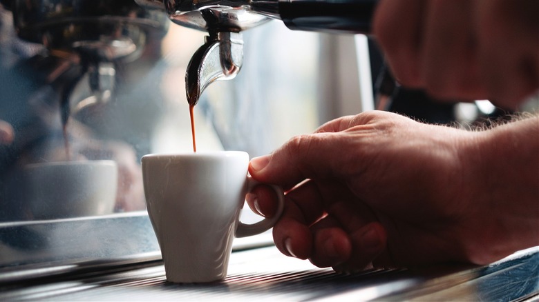 A close-up of a man brewing a shot of espresso into a white cup