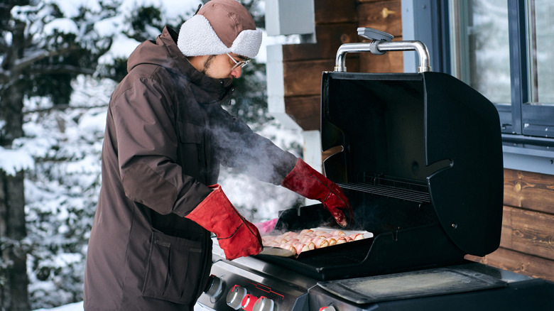 Man outside grilling in the snow.
