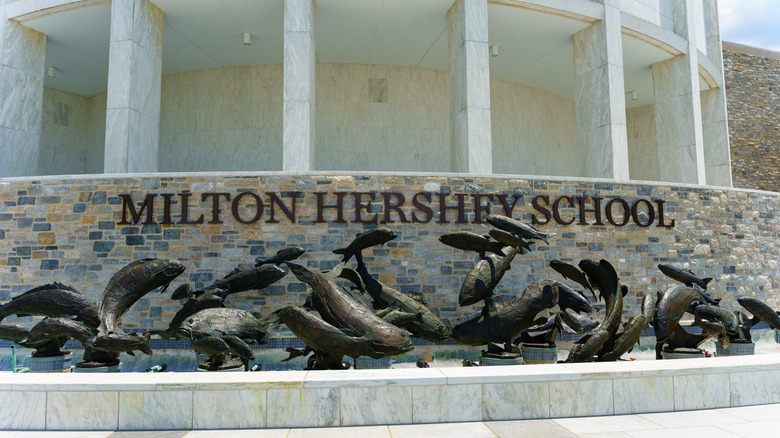 Milton Hershey School sign on brick wall, statues in front