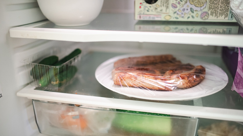 A plate of leftover sausages wrapped in plastic wrap on a shelf in the fridge