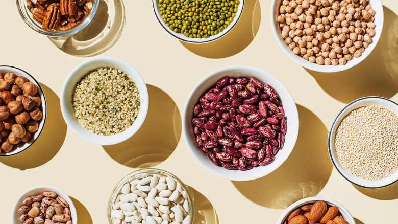Various beans, nuts, and legumes in white bowls on a beige background