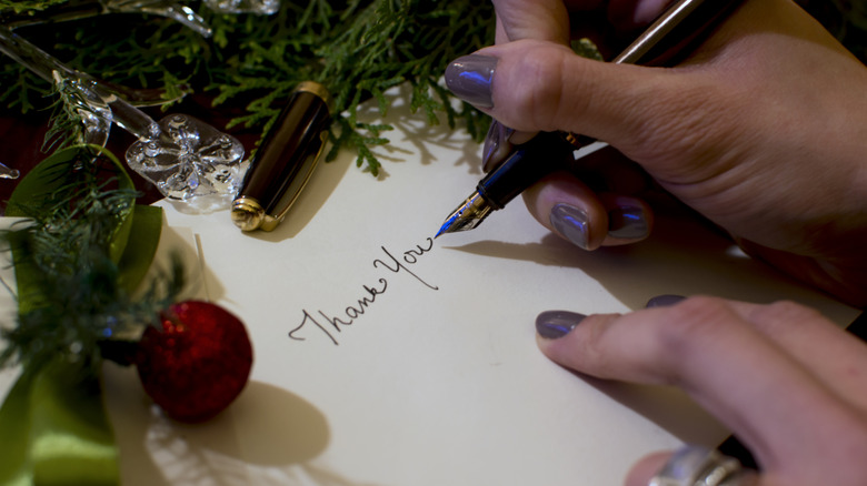 person writing thank you on a card with Christmas decorations on table