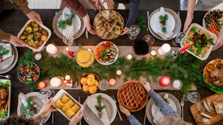 Top view of multiple hands arranging large number of dishes on holiday table