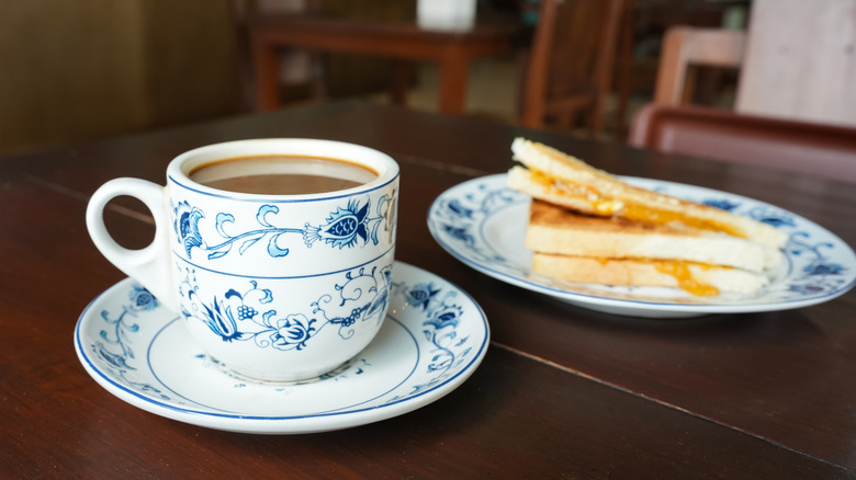 Blue porcelain cup of kopi cham coffee drink next to plate of kaya toast