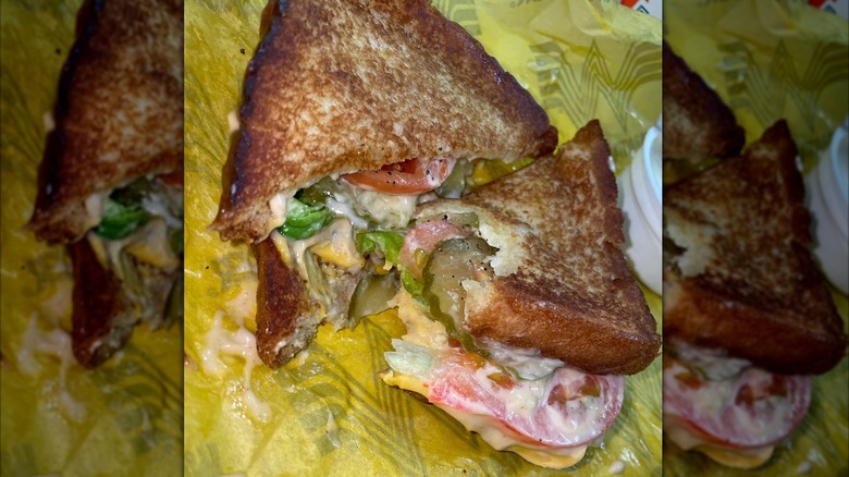 Close-up of grilled cheese on toast with lettuce, tomatoes, pickles, and sauce