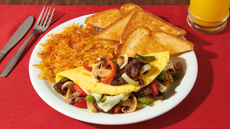 Denny's Philly cheesesteak omelet on white plate and red placemat