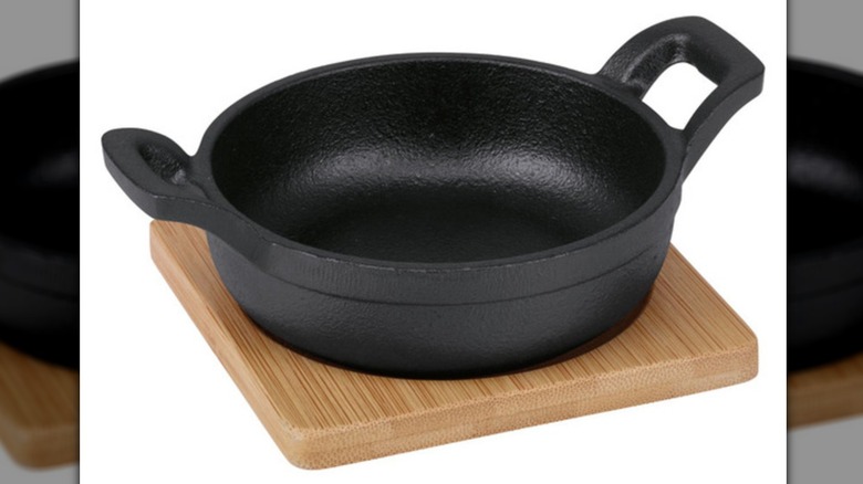 Black cast iron mini skillet with two handles sitting on wooden trivet