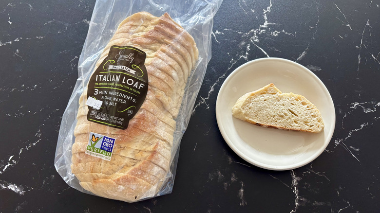 Aldi Specially Selected Italian loaf sliced inside a bag next to a slice of bread on a plate against a black marble counter