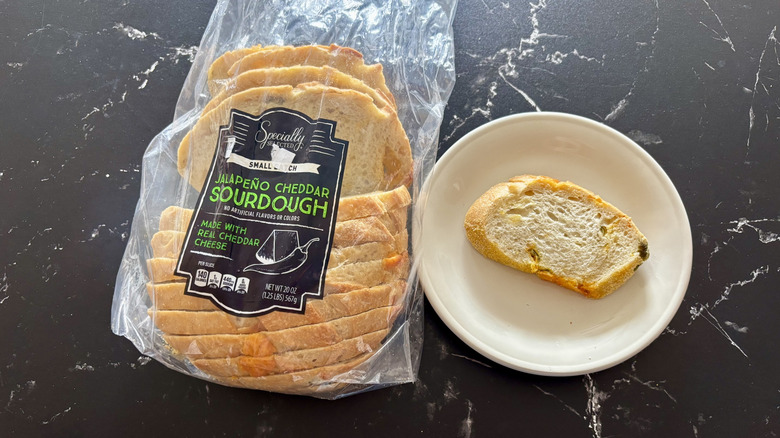 Aldi Specially Selected jalapeño cheddar sourdough in a bag next to slice on plate on a black marble counter