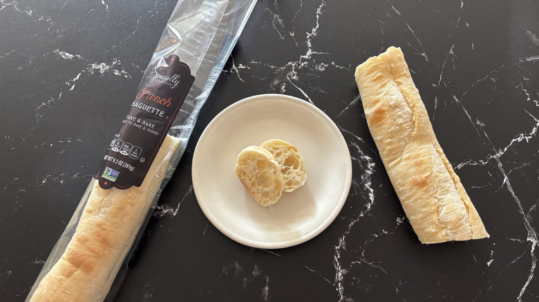 Aldi French baguette next to slices on plate and bigger piece of baguette all laid on a black marble counter