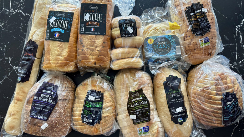 Various Aldi brand bread loaves, naan, and bagels packed in bags and lined on a black marbled countertop