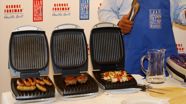several foreman grills cooking food with George Foreman standing beside