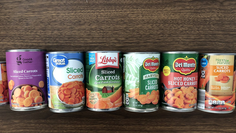 10 different brands of canned carrots in a line.