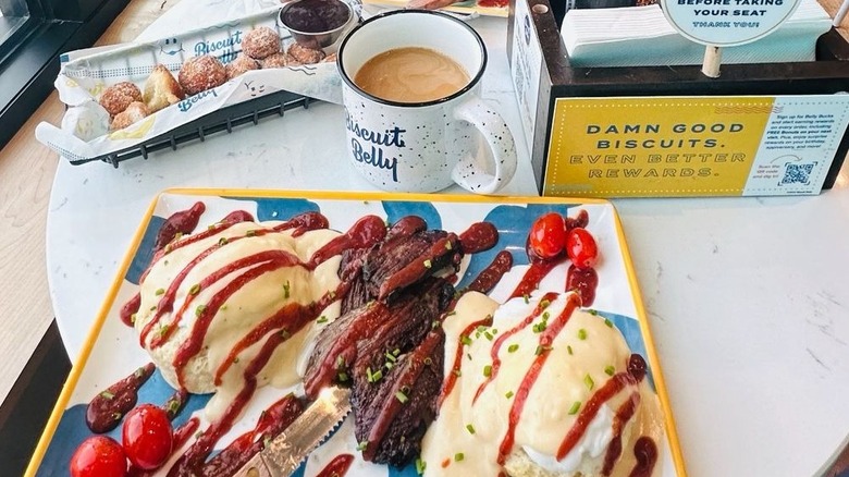 Eggs benedict served on biscuits, alongside coffee and Bonuts on table at Biscuit Belly