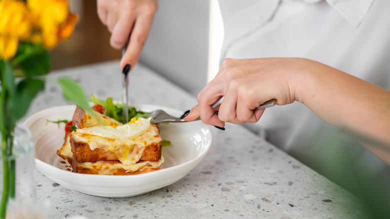 Woman's hands cutting into toast with cheese, egg, and arugula