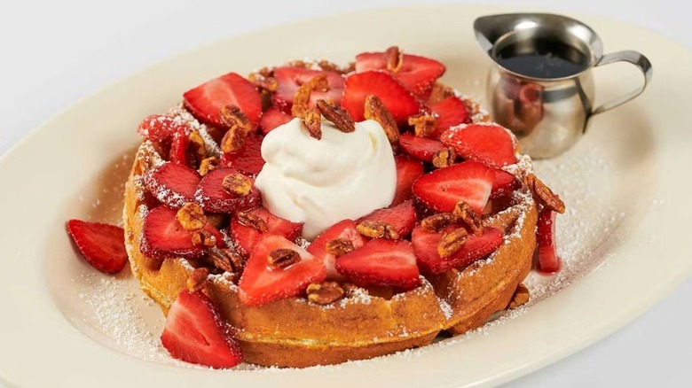 Giant Belgian waffle topped with pecans, strawberries, and Chantilly cream, served alongside maple syrup