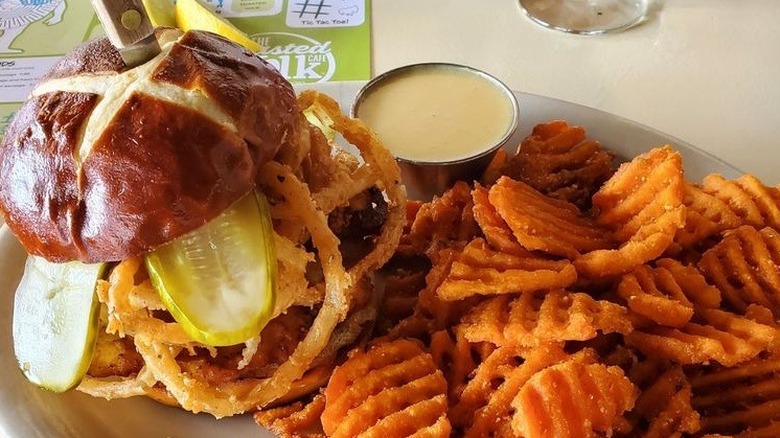 Fried chicken sandwich with pickles served on pretzel bun alongside sweet potato fries served at The Toasted Yolk Cafe