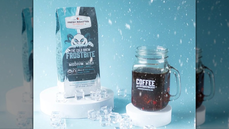 Bag of Frostbite Cold Brew Coffee on blue background next to handle mason mug of iced coffee
