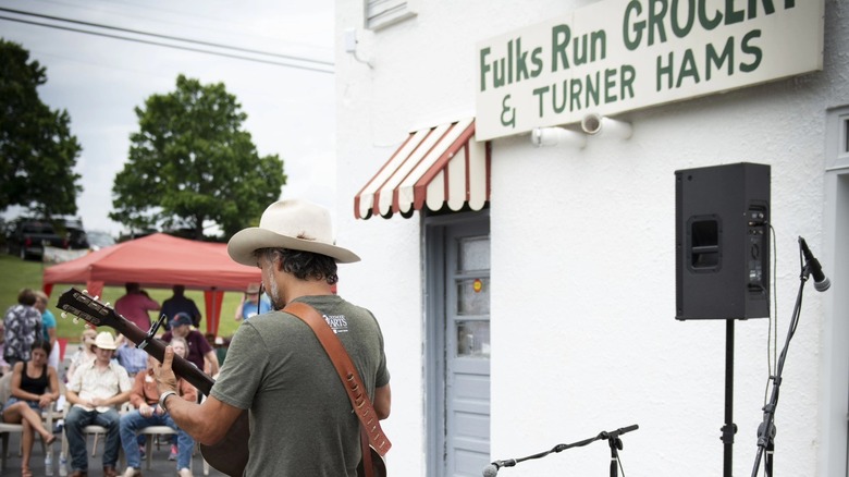 Man playing guitar in front of Fulks Run Grocery & Turner Hams sign