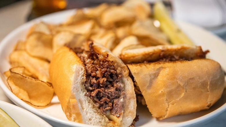 Two halves of a cheesesteak on plate with potato chips
