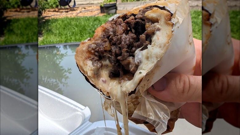Hand holding half of a cheesesteak outside with stretchy cheese
