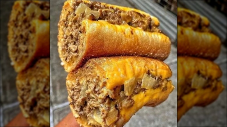 Hand holding two halves of a cheesesteak