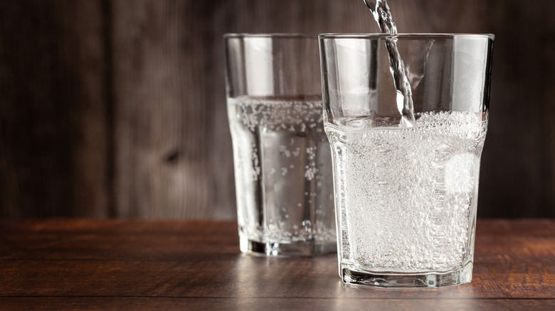 Person pouring sparkling soda water into a tall glass