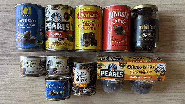 Variety of packaged black olives on wooden table
