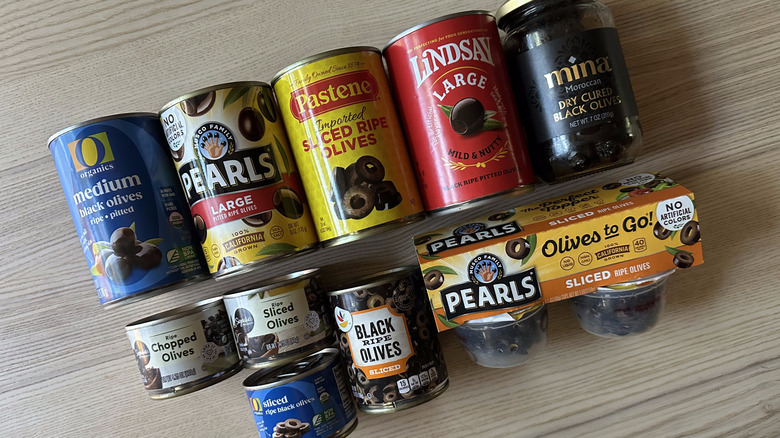 Variety of packaged black olives on wooden table