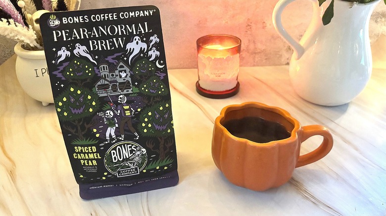 Bones Coffee Pear-anormal Brew bag next to pumpkin mug of black coffee, candle and vases in background