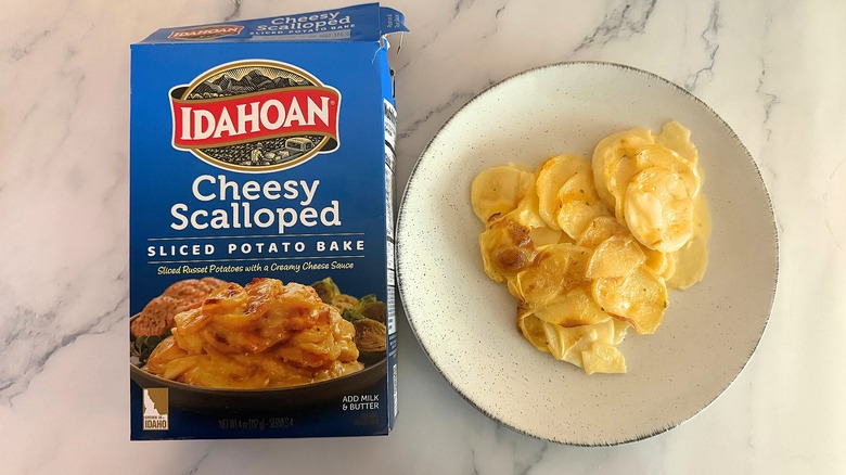 Box of Idahoan Cheesy Scalloped Potatoes next to scalloped potatoes on white plate