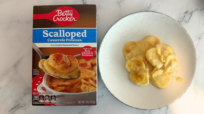 Box of Betty Crocker Scalloped Potatoes next to scalloped potatoes on white plate