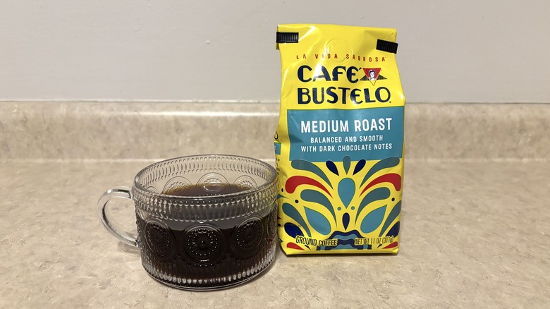 Cafe Bustelo medium roast ground coffee in bag and glass mug on neutral background.