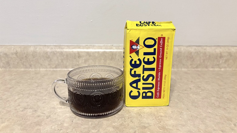 Cafe Bustelo classic ground coffee in brick and glass mug on neutral background.