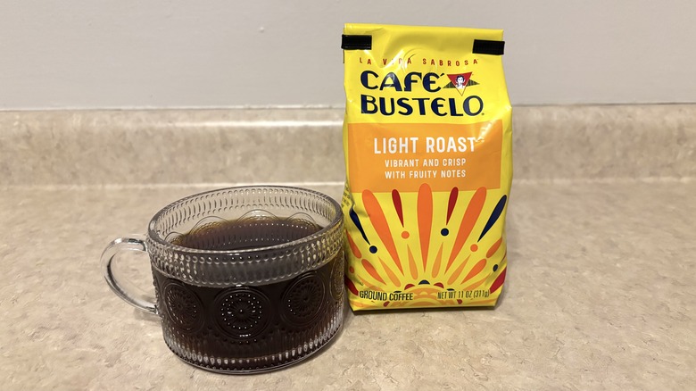 Cafe Bustelo light roast ground coffee in bag and glass mug on neutral background.