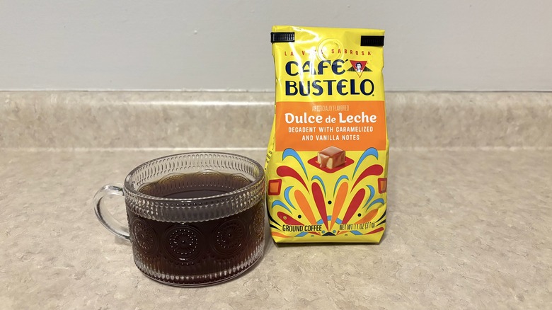 Cafe Bustelo dulce de leche ground coffee in bag and glass mug on neutral background.