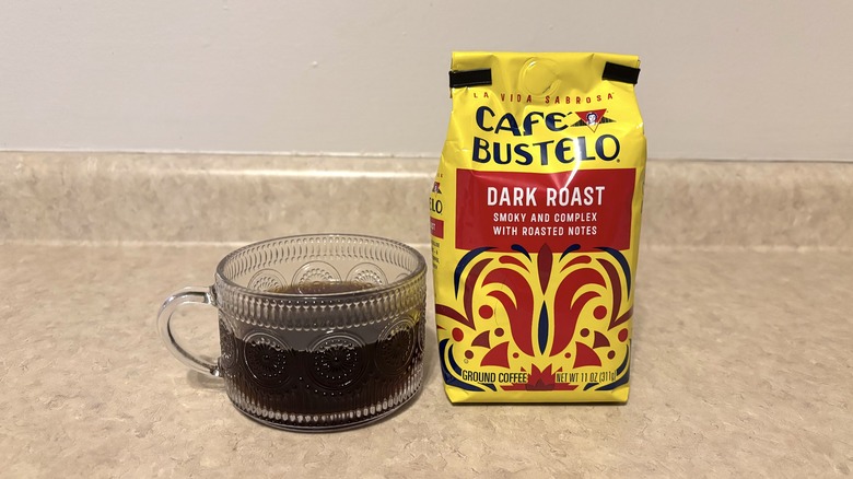 Cafe Bustelo dark roast ground coffee in bag and glass mug on neutral background.