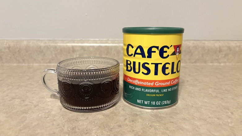 Decaffeinated Cafe Bustelo ground coffee in can and glass mug on neutral background.