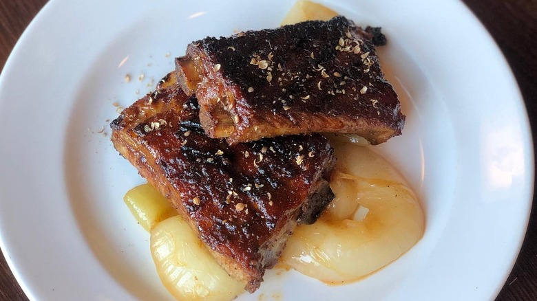 Glazed ribs stacked on top of each other, sprinkled with pepper flakes on a white plate