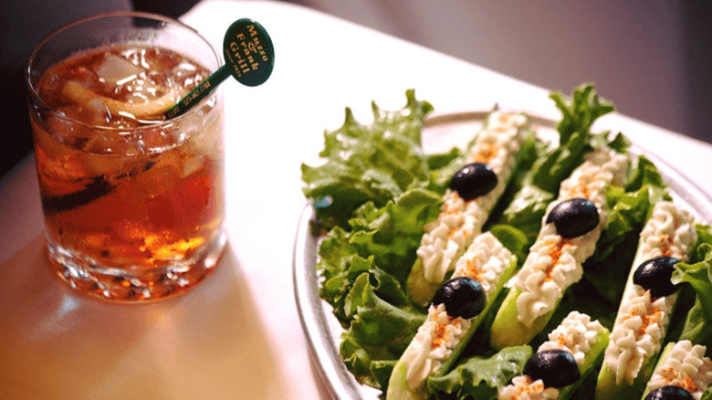 Stuffed celery stalks arranged on a platter over fresh lettuce, sitting next to a whiskey cocktail with a stirrer labeled "Musso & Frank Grill" in it